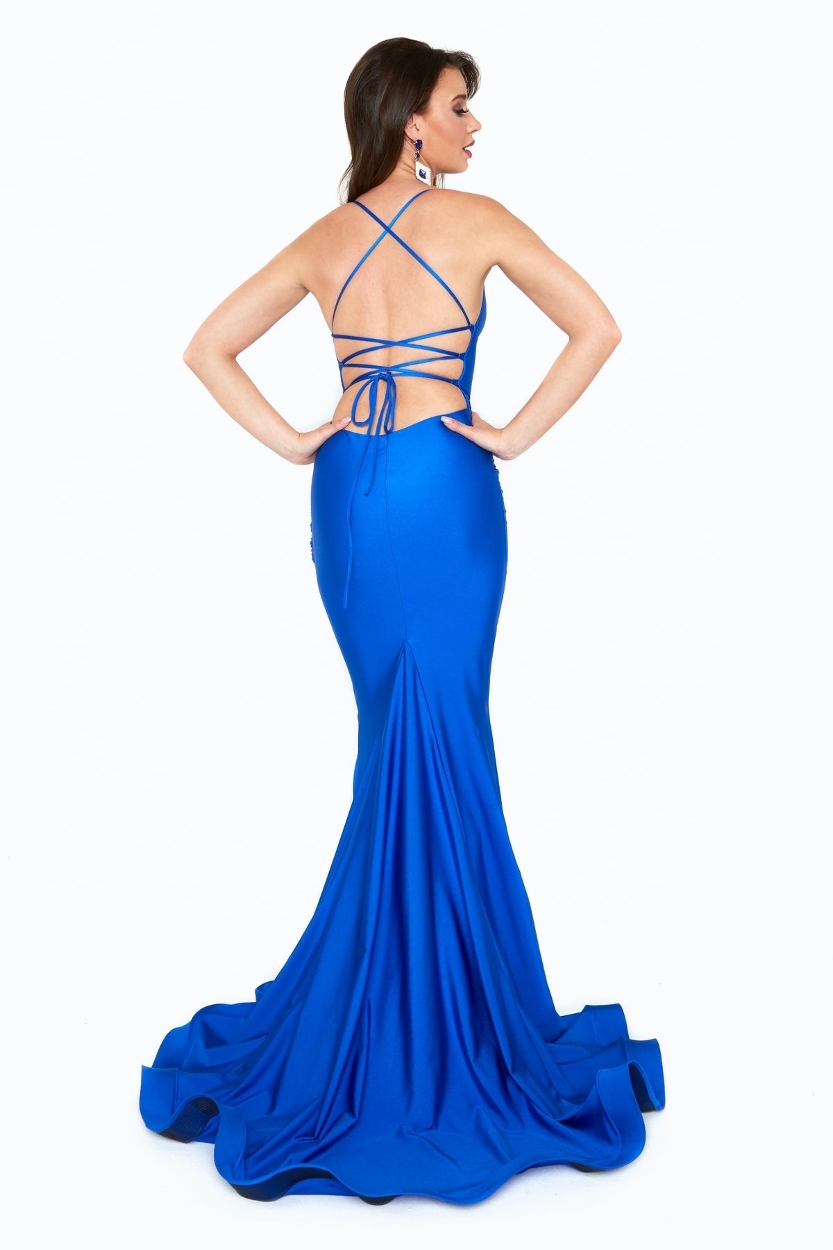 Woman in the Ruched Empire-Waist Long Mermaid Prom Dress (6536H), floor-length royal blue with open back, crisscross straps, slight train, standing hands on hips.